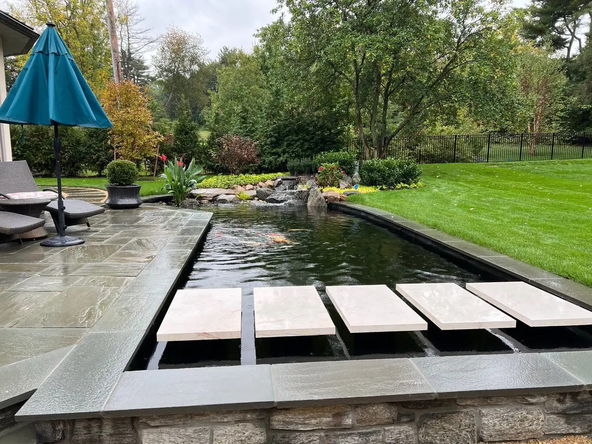 Finished koi pond with clear circulating water, stepping stones, plants, and a waterfall